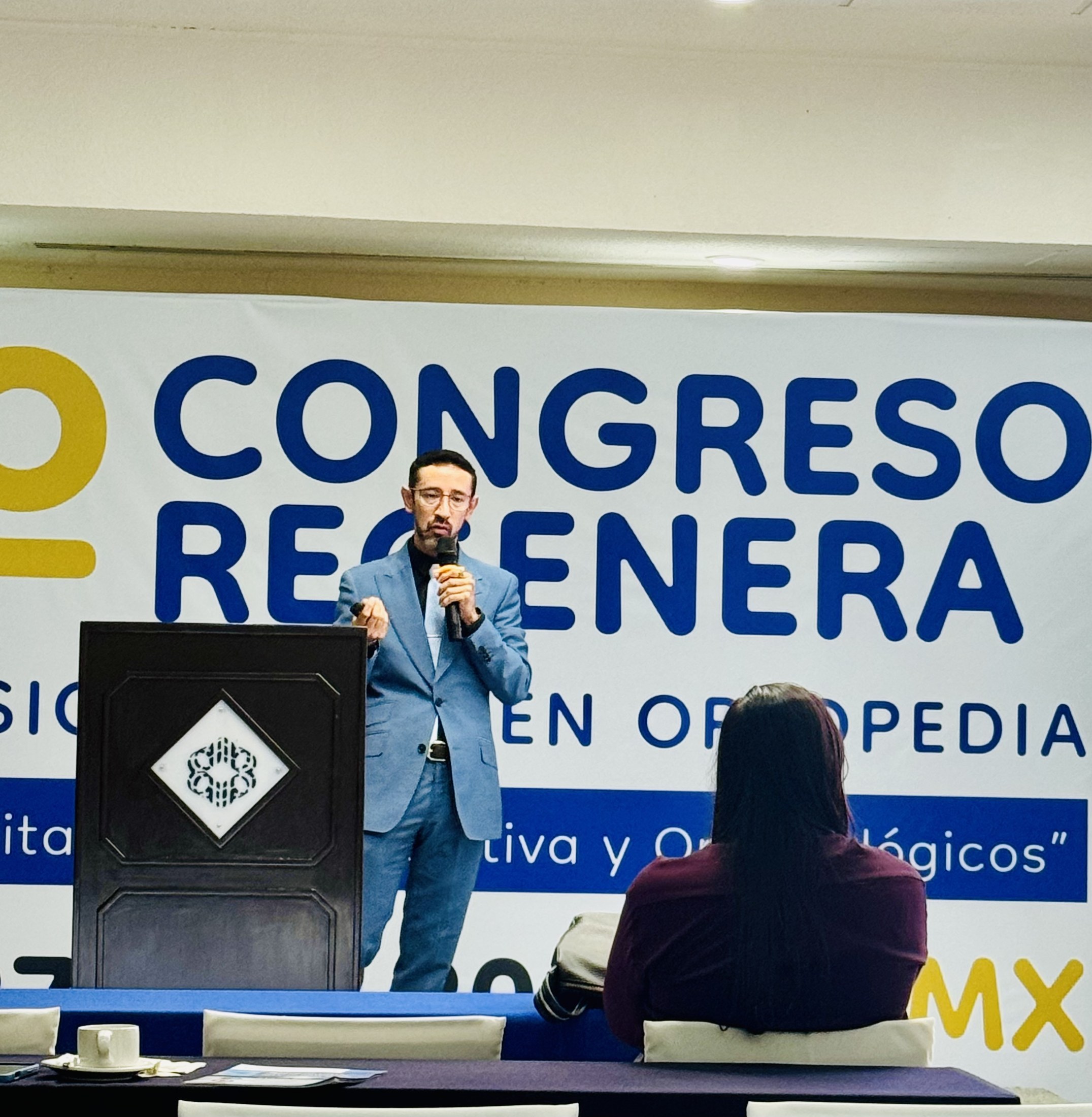 Ponente con micrófono frente a la lona del 1.er Congreso REGENERA.